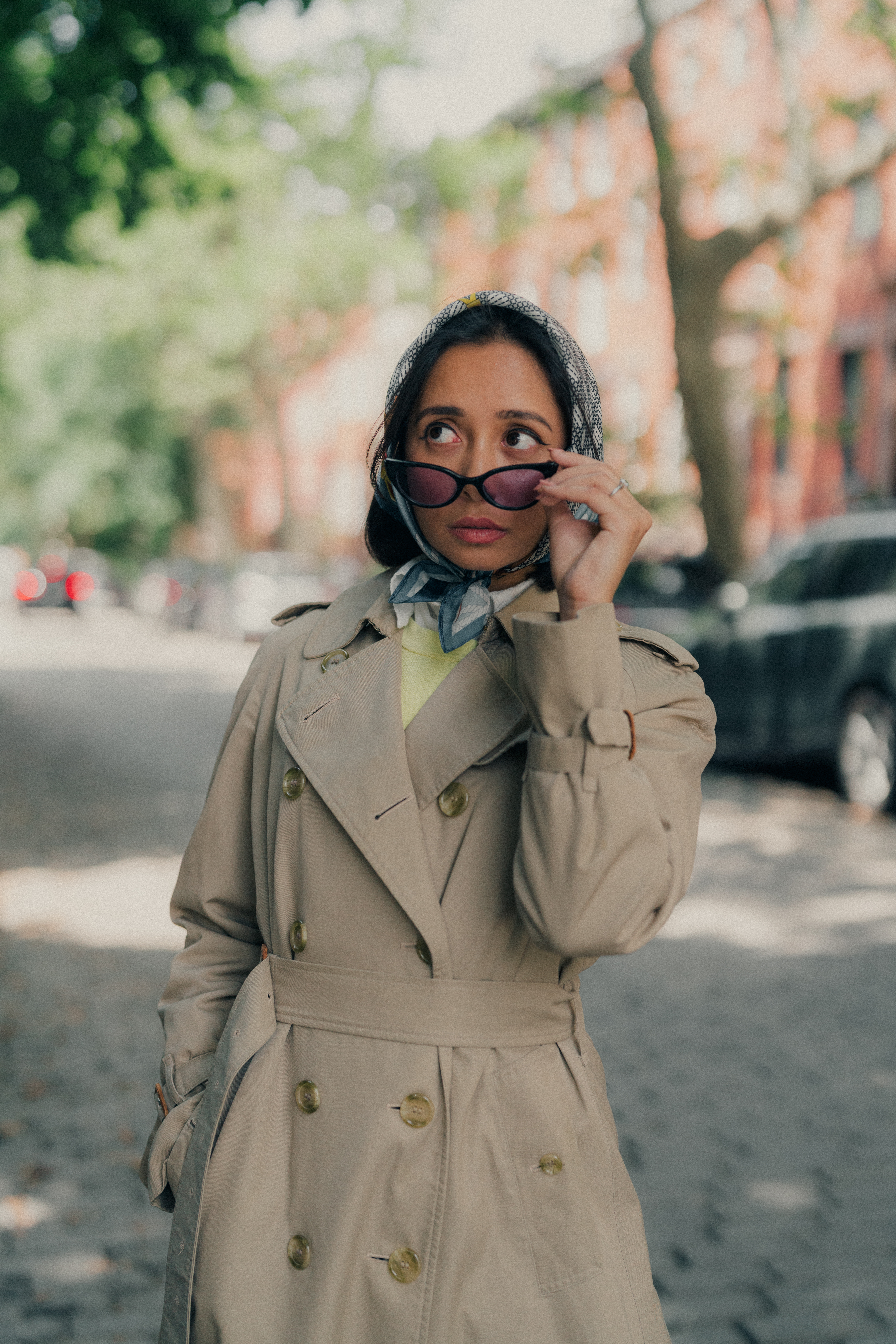 Raisa Ahmed in a tan trench coat, headscarf, and sunglasses